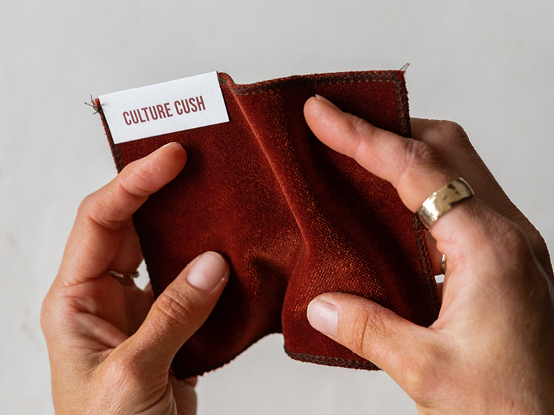 Hands holding a fabric swatch with a Culture Cush label – Newcastle brand specialising in custom modular lounges.
