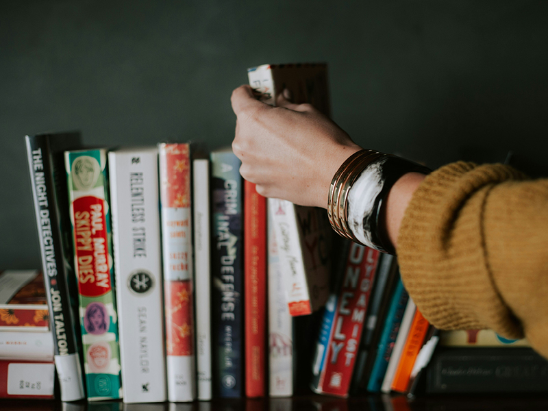 A person reaching for a book on a crowded bookshelf, highlighting the idea of making time for reading in everyday life.
