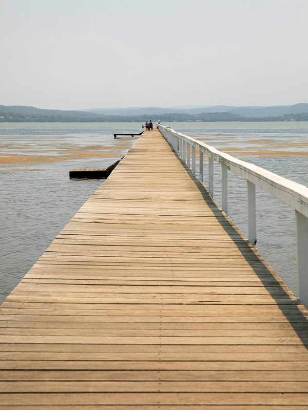 The wooden boardwalk at Long Jetty on the Central Coast, stretching into Tuggerah Lake with people at the end.