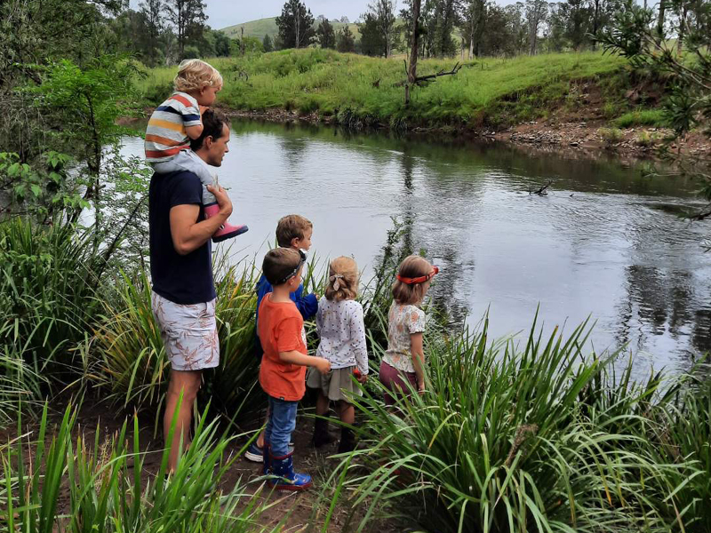 Father and children on a family holiday standing by a river, enjoying nature.