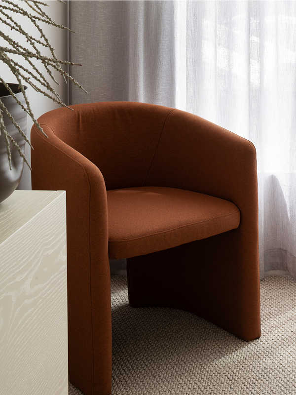 Rust-coloured accent chair by Mojo Homes styled beside a window with neutral curtains.