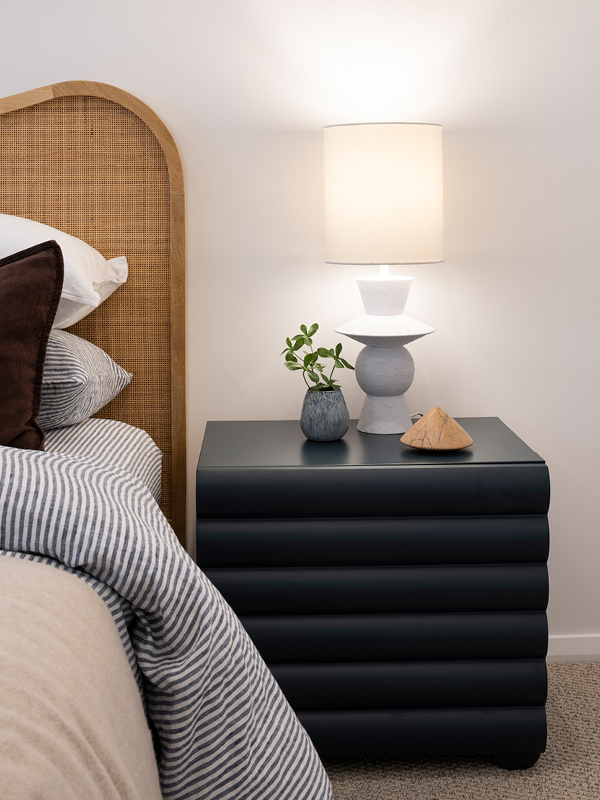Mojo Homes bedroom with rattan bedhead, striped linen and a modern bedside lamp.