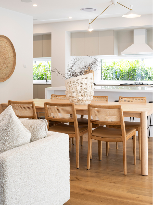 Mojo Homes dining and kitchen with rattan chairs, white cabinetry and a window splashback bringing greenery inside.