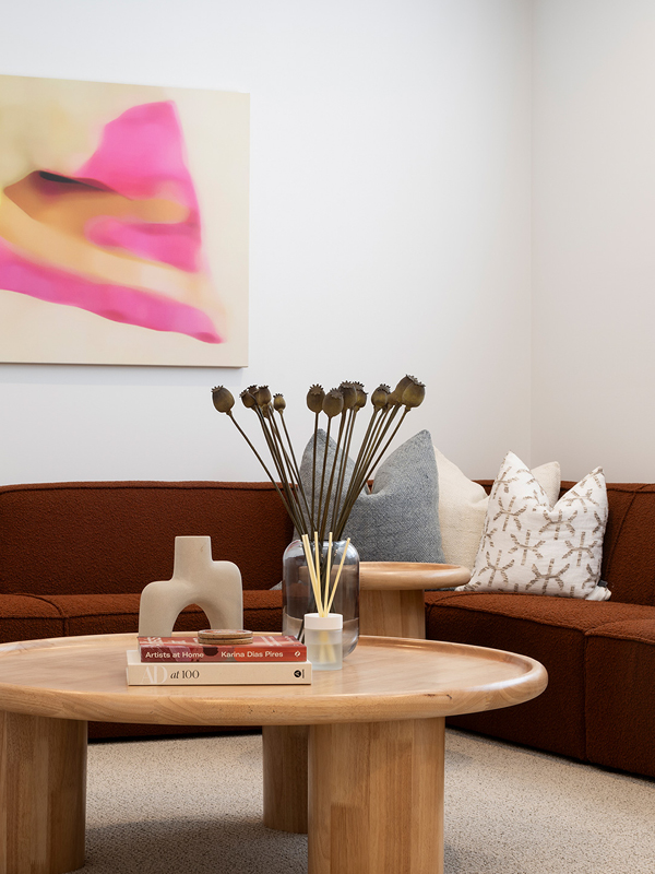 Mojo Homes lounge room with brown modular sofa, round timber tables and bold artwork adding colour.