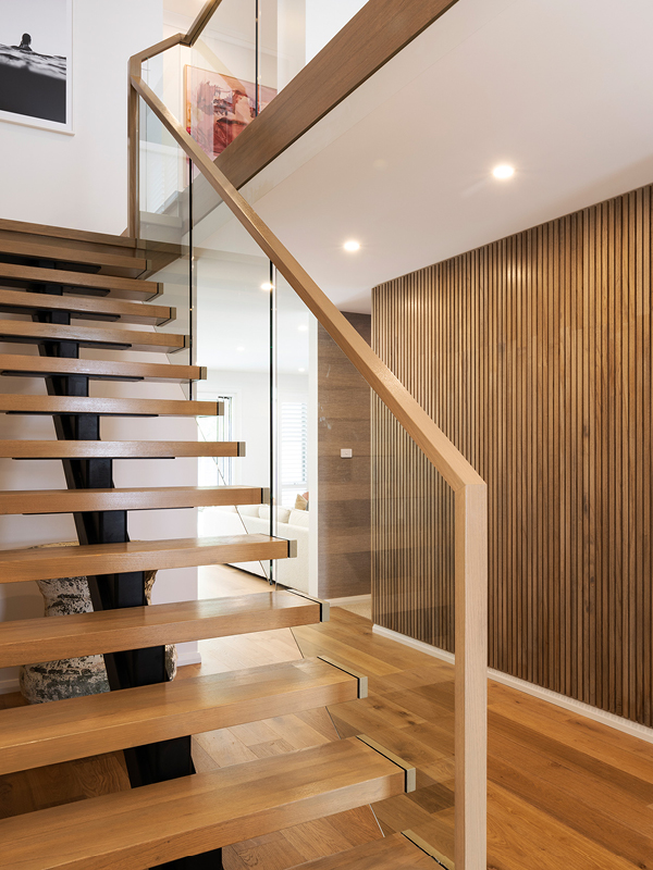 Modern staircase in a Mojo Homes build with timber treads, glass balustrade and timber feature wall.