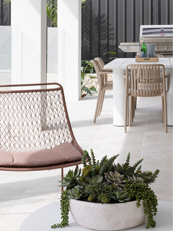 Outdoor entertaining area in a Mojo Homes build with dining table, lounge chair and greenery.