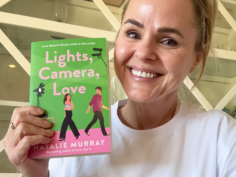 Newcastle author Natalie Murray holding her new romance novel Lights, Camera, Love.
