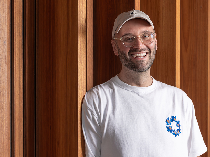 Reece Hignell, owner of Acacia Dining in Maitland, smiling in front of a timber wall.